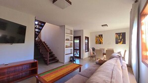 Ein geräumiges Wohnzimmer mit Treppe, Flachbildfernseher, Sofa und Kunstwerken an den Wänden.