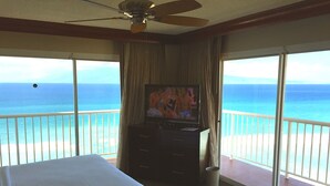 A hotel room with a large bed, a television, and a balcony with a view of the ocean.
