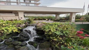 A waterfall in a landscaped area with a bridge overhead.