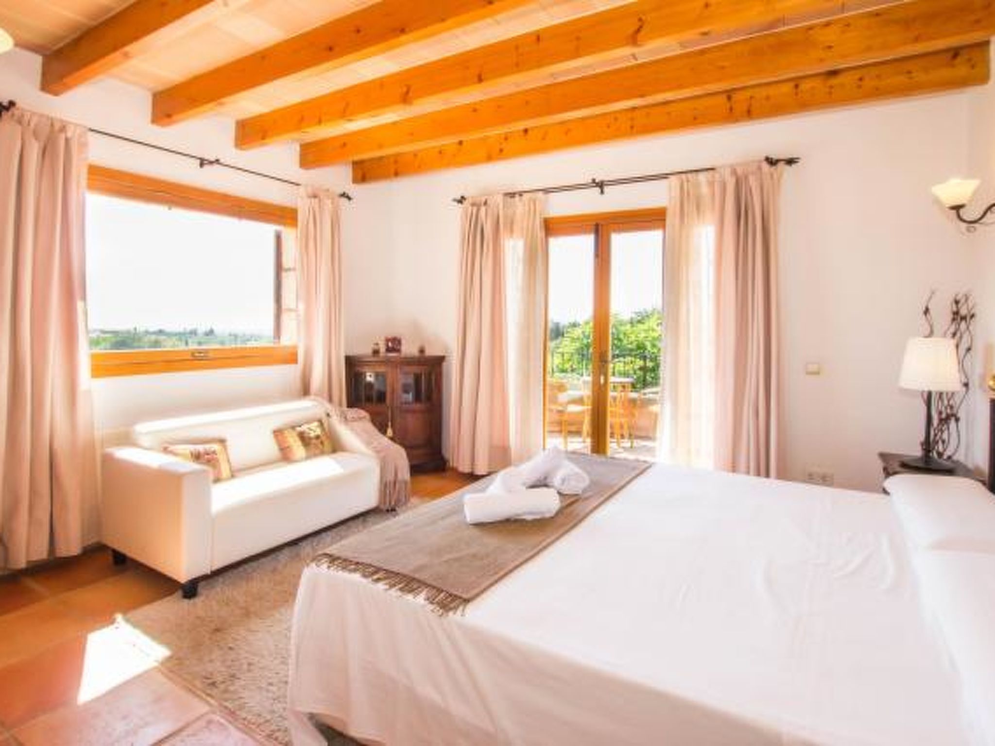 A bedroom with a bed, a sofa, a wooden ceiling, and a view through a window.