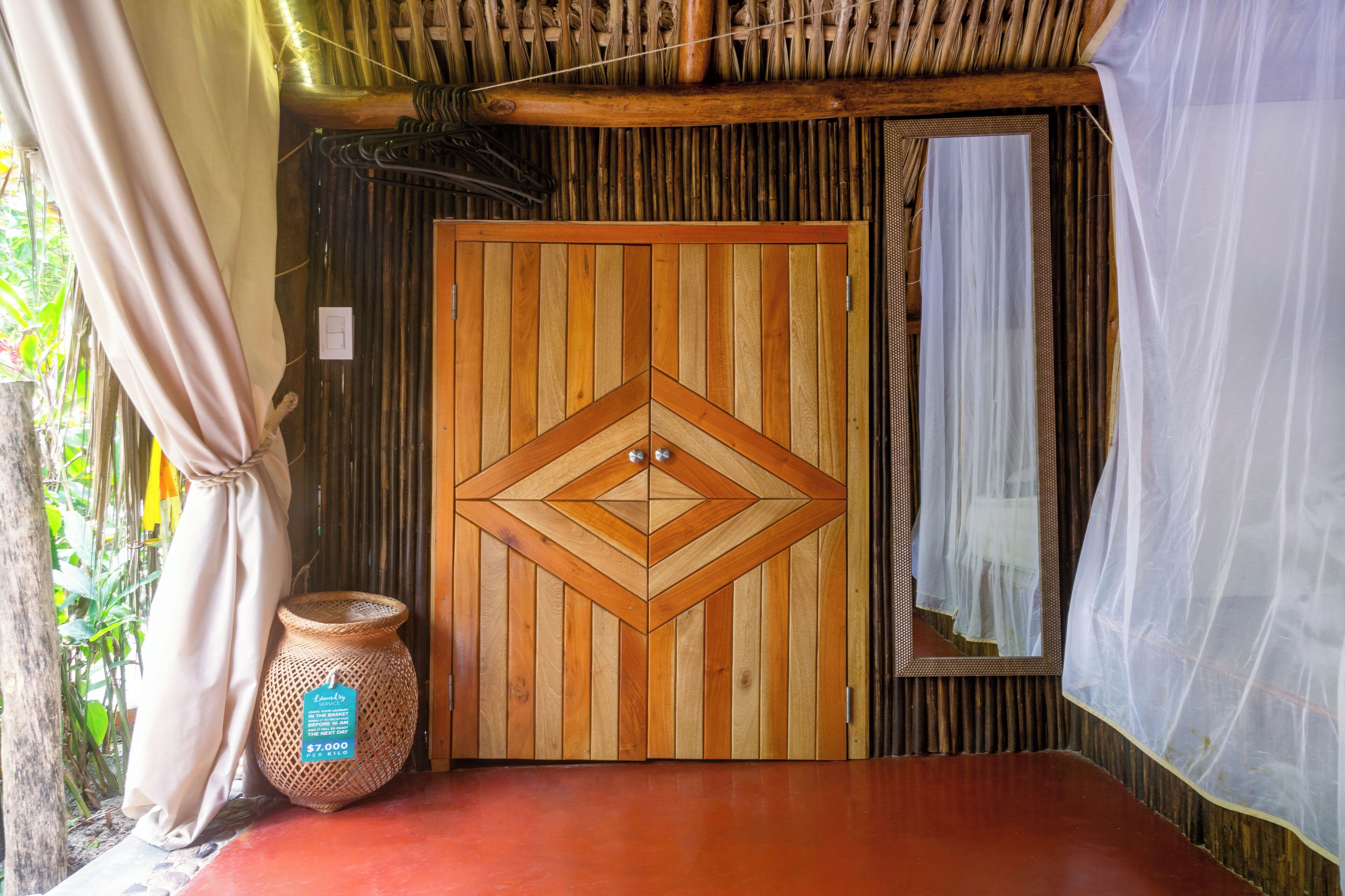 Una habitación con una puerta de madera decorada con un diseño geométrico, una cesta tejida y un suelo rojo.