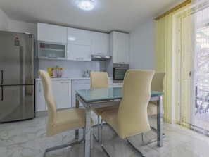 A modern kitchen with a refrigerator, oven, and dishwasher. There is a dining table with four chairs. - KOTVICA / HR-10106-01 by Interhome (Selce)