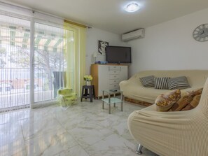A living room with a sofa, a TV, a small table, and a sliding glass door. - KOTVICA / HR-10106-01 by Interhome (Selce)