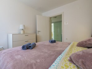 A bedroom with a bed, a bedside table with a lamp, and a door leading to another room. - KOTVICA / HR-10106-01 by Interhome (Selce)