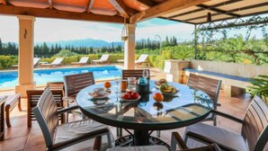 A covered outdoor dining area with a pool view, wooden furniture, and a glass table. - Blaypetit by Interhome (Muro)
