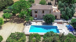 Una casa de pedra amb piscina, envoltada d'arbres i camps oberts.