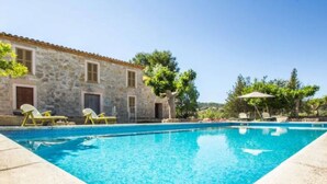 Edifici de pedra amb piscina, gandules i arbres.