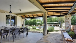 Une terrasse extérieure dotée d’un espace salon abrité, d’une piscine et d’un mur en pierre.