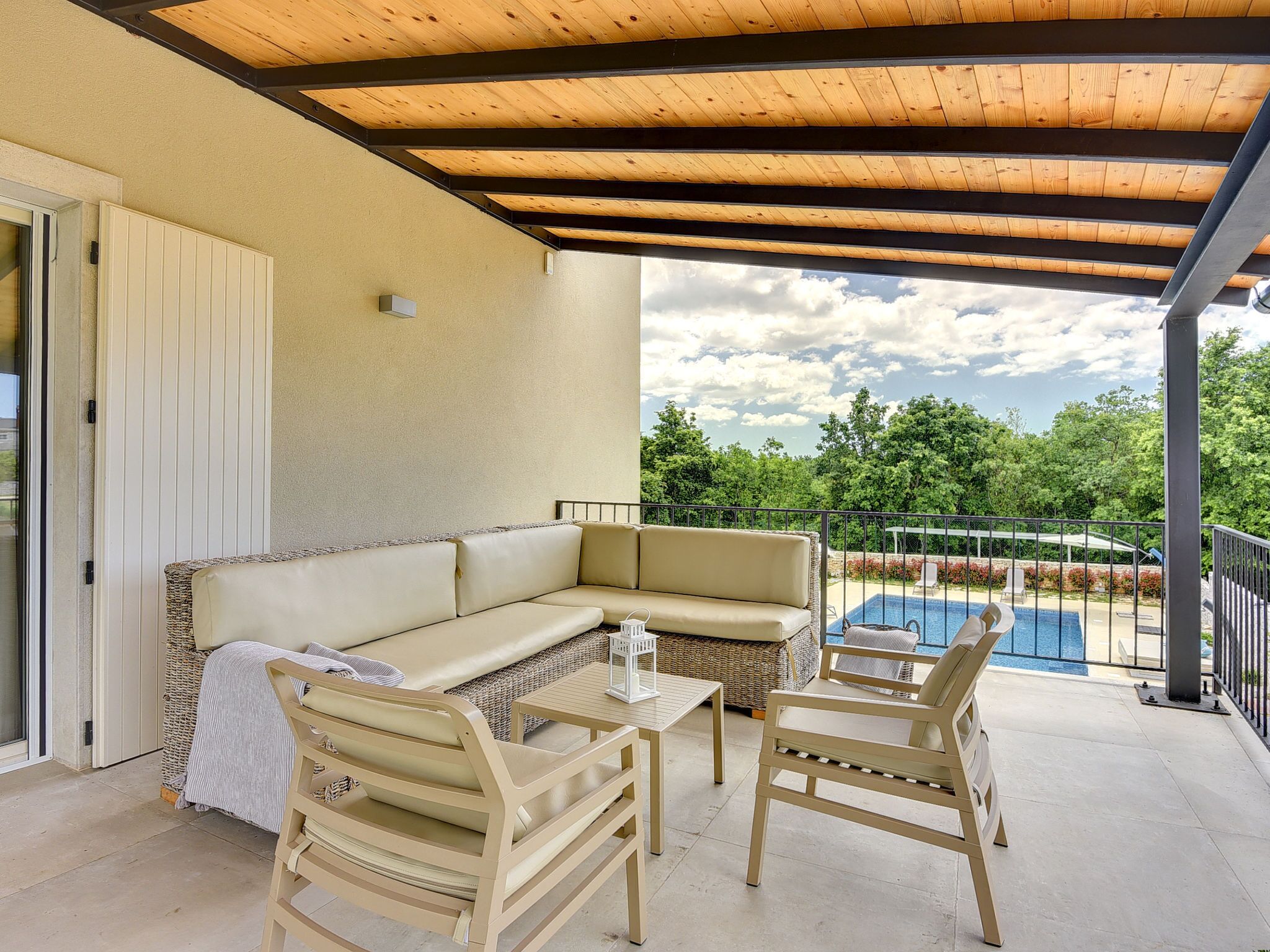 Un espacio de estar al aire libre cubierto con un sofá, sillas y una mesa, con vistas a una piscina y follaje.