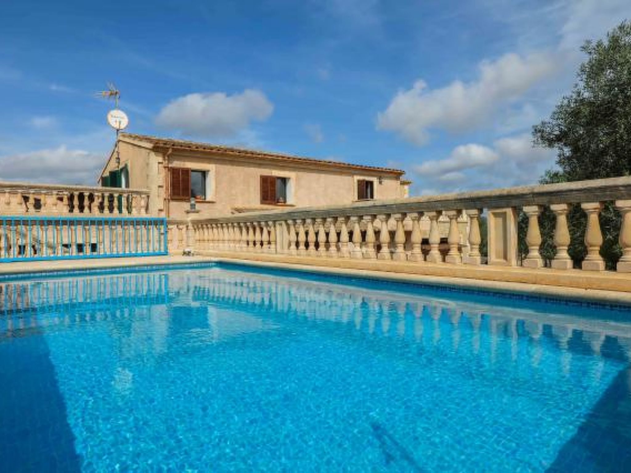 A swimming pool with a balustrade, a building with a tiled roof, and a clear sky.