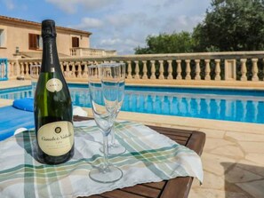 A bottle of wine and two glasses on a table by a pool with a building in the background. - Vacation home Cogol by Interhome (Manacor)