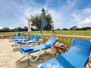 A row of blue lounge chairs with white frames and blue cushions, arranged on a stone patio with a wooden railing. - Vacation home Cogol by Interhome (Manacor)