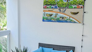 Et værelse med en fletsofa, et glastæppe, en potteplante og et maleri af en strandscene.