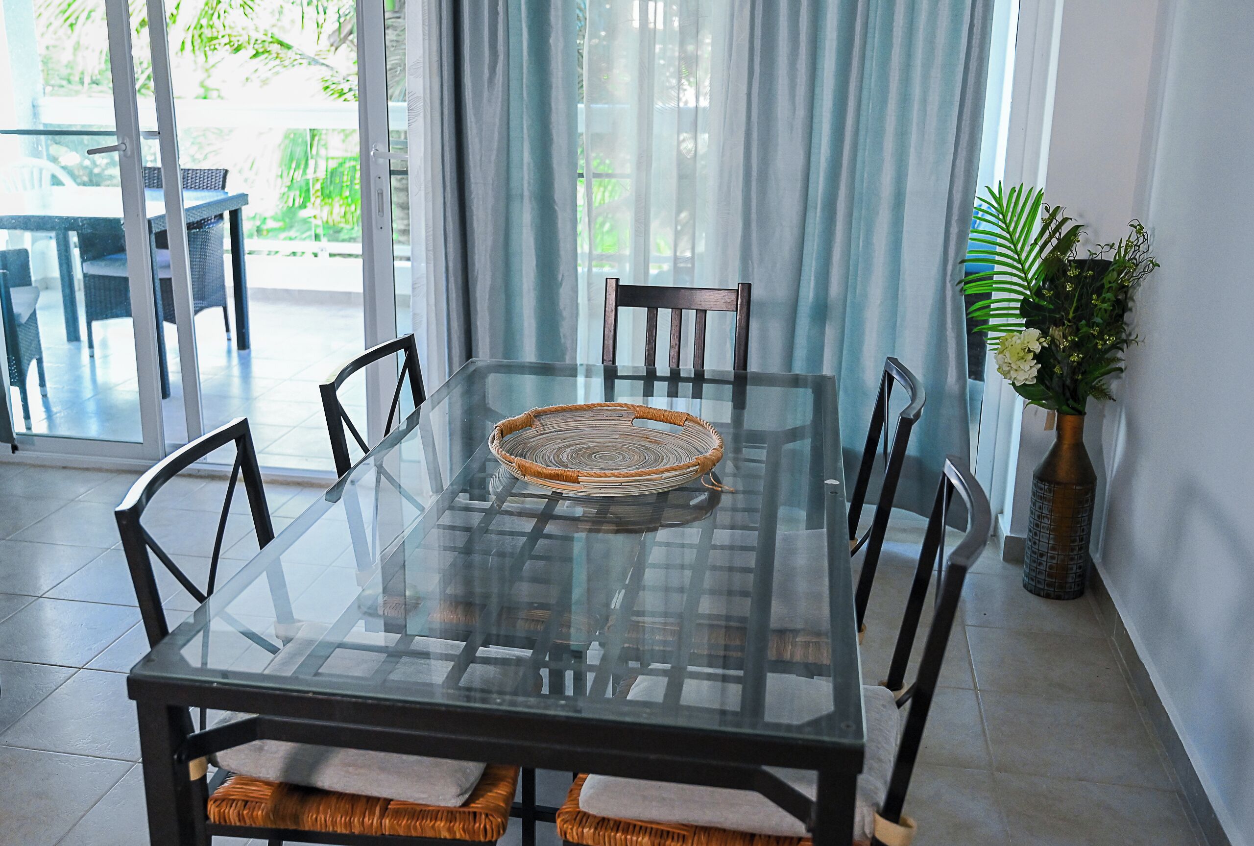 A glass-top dining table with woven placemats, surrounded by dark chairs with cushioned seats.