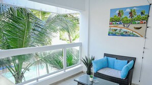 En balkon med en fletsofa, et glasbord og en potteplante.