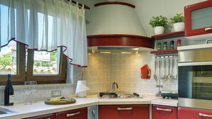 A kitchen with red cabinets, a stove, a microwave, and a window with curtains. - Villa Maria Betiga by Interhome (Barbariga)