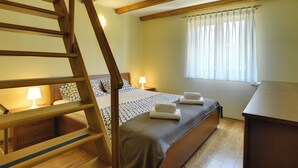 A bedroom with a wooden staircase, a bed with patterned bedding, bedside lamps, and a window with sheer curtains. - Villa Maria Betiga by Interhome (Barbariga)