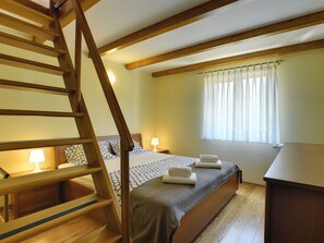 Ein Schlafzimmer mit einer Holztreppe, einem Bett mit gemusterten Betttextilien, Nachttischlampen und einem Fenster mit durchsichtigen Vorhängen.