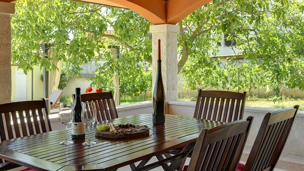An outdoor patio with a wooden table, chairs, a bottle of wine, and a glass. - Villa Maria Betiga by Interhome (Barbariga)