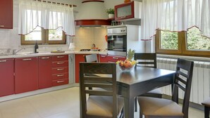 A kitchen with red cabinets, a dining table with chairs, a built-in oven, and a window with curtains. - Villa Maria Betiga by Interhome (Barbariga)
