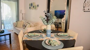 Ein Essbereich mit einem runden Tisch, gedeckt für vier Personen, einer Blumenvase und einer Couch im Hintergrund.