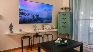 Ein Wohnzimmer mit Fernseher an der Wand, einem kleinen Tisch mit Tablett und einem türkisblauen Schrank mit Schubladen.