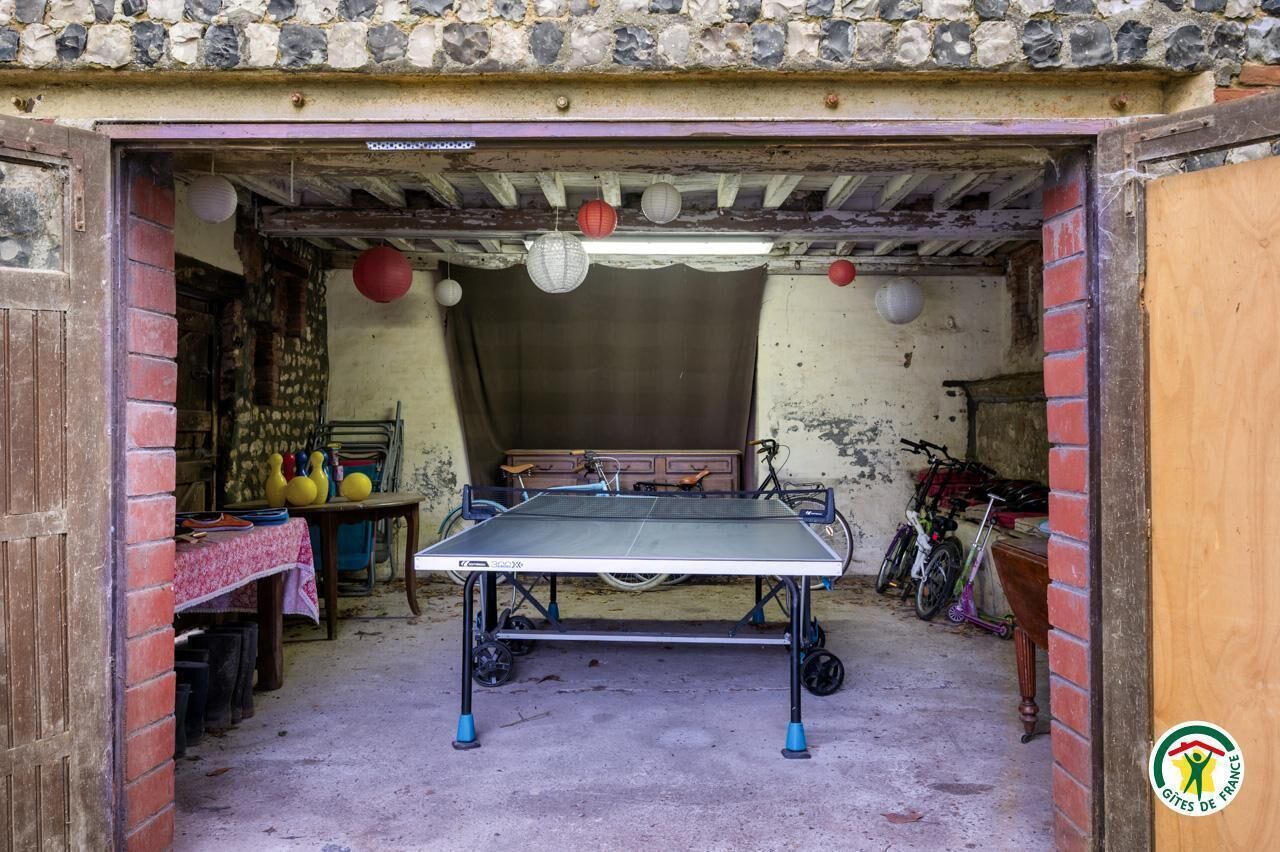 Una mesa de ping pong en una habitación rústica con paredes de ladrillo, techo de madera y varias bicicletas y objetos en el fondo.