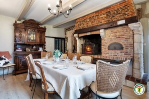 A dining area with a brick fireplace, wooden furniture, and a chandelier. - Gîtes de France® - La Chaumière Normande (BEAUREPAIRE)