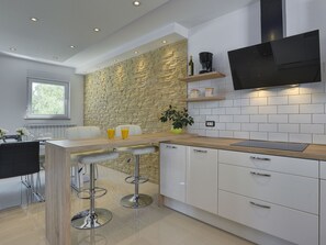 A modern kitchen with a stone wall backsplash, a wooden bar counter, and a built-in TV. - Villa Zeus by Interhome (Bokordici)
