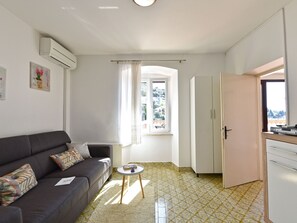 A compact living space with a sofa, a small round table, a kitchen area, and a window with a view. - Apartment 1825 by Interhome (Rabac)
