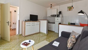 Ein gemütlicher, kleiner Wohnraum mit Küchenzeile, einer Couch, einem Tisch und einem Fernseher.
