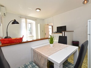 A compact living space with a kitchenette, a dining area with a table and chairs, a television, and a window with curtains. - Apartment 1825 by Interhome (Rabac)