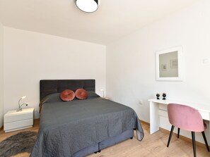 Une chambre à coucher moderne, comprenant un lit, une table de chevet, un bureau, une chaise et un petit miroir.