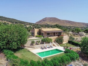 Uma casa com piscina, rodeada por vegetação e uma montanha ao fundo.
