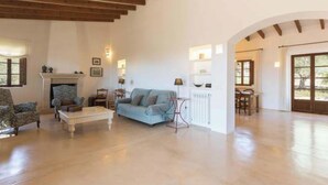 A spacious living room with a fireplace, a sofa, a coffee table, and a dining area. - Vacation home Calma by Interhome (Sant Llorenç des Cardassar)