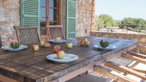 A wooden table with plates of apples and two chairs, set against a stone wall with green shutters. - Vacation home Calma by Interhome (Sant Llorenç des Cardassar)