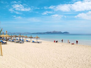 A beach with sun loungers and thatched umbrellas, a clear sky, and a calm sea. - Mariposa by Interhome (Muro)