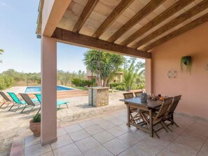 Eine überdachte Terrasse mit Pool, Sitzgelegenheiten im Freien und Blick auf die umliegende Landschaft.
