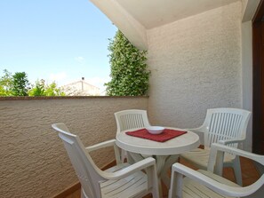 Un balcone con un tavolo bianco e quattro sedie bianche, un sottopiattino rosso e una pianta verde.