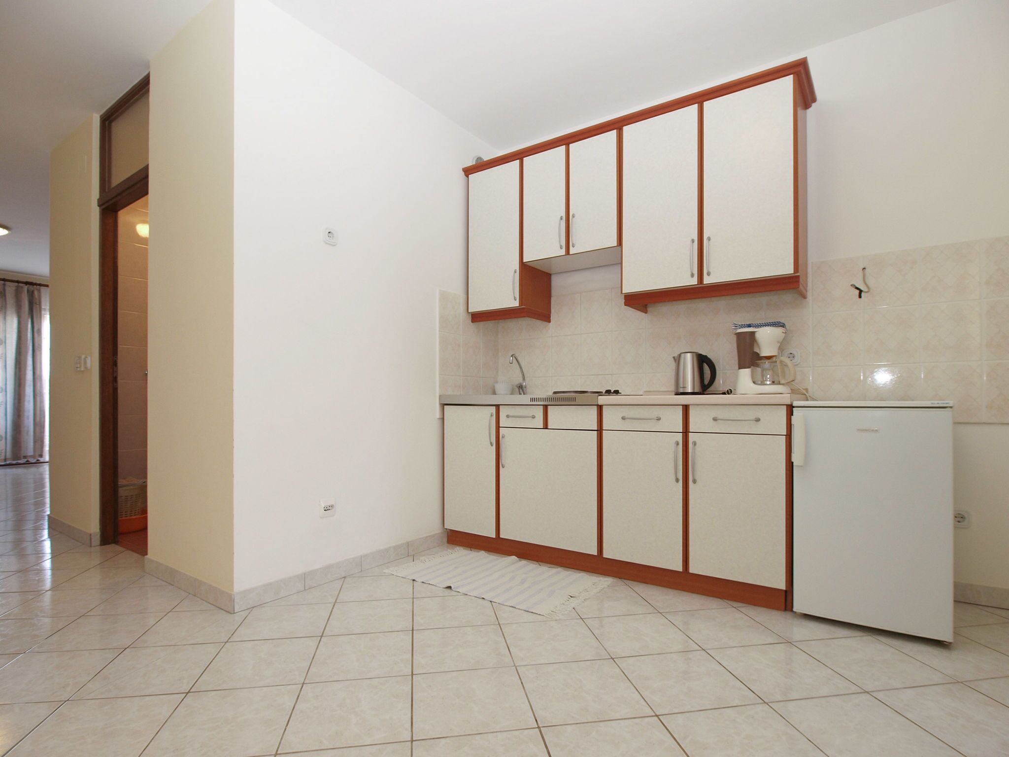 Una cocina con armarios blancos, un refrigerador, una tetera y una cafetera.