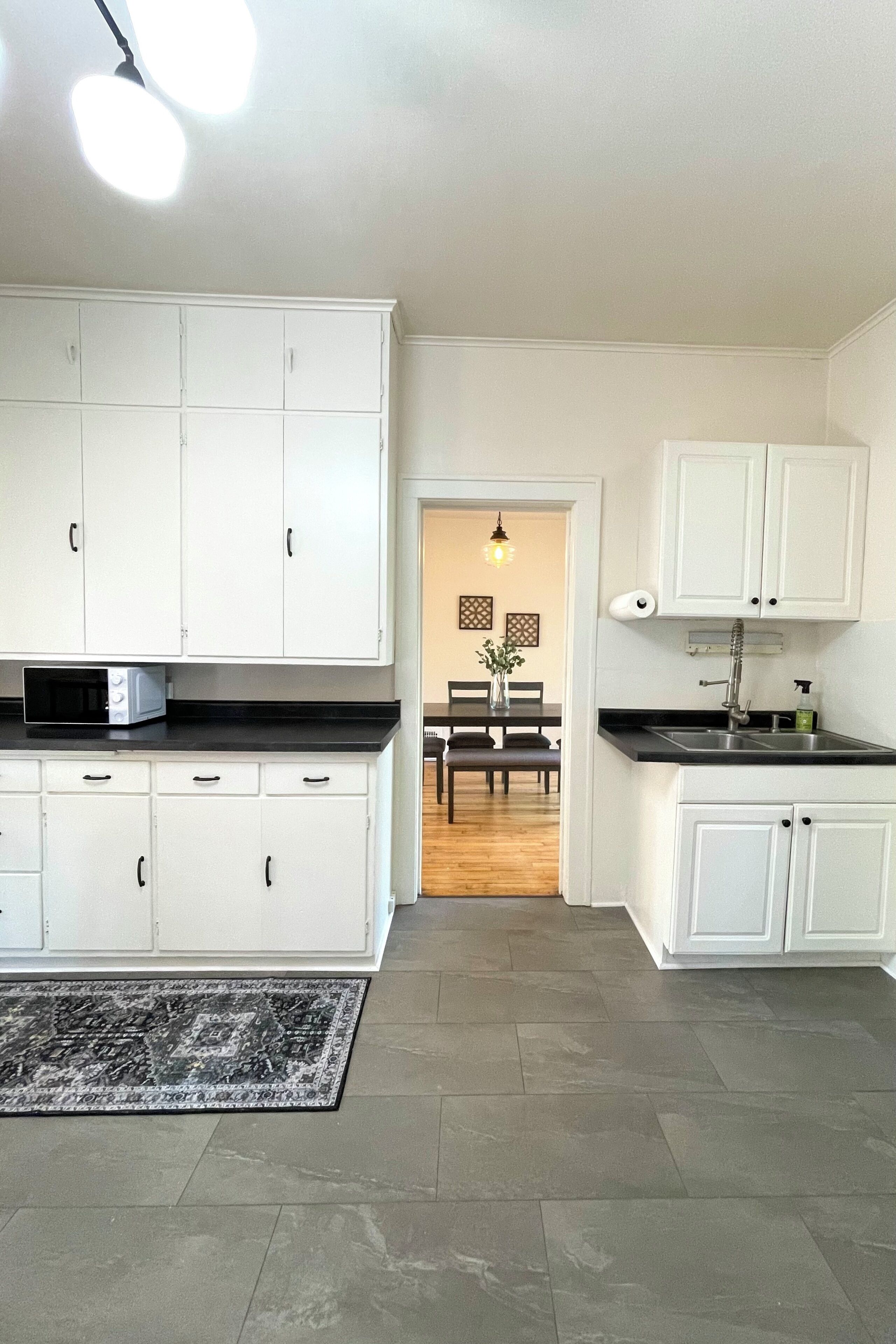 A modern kitchen with white cabinets, a black countertop, and a dining area visible in the background.