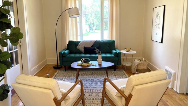 Ein Wohnzimmer mit einem grünen Sofa, zwei weißen Sesseln, einem Couchtisch, einer Stehlampe und einem kleinen Beistelltisch mit einer Schale.