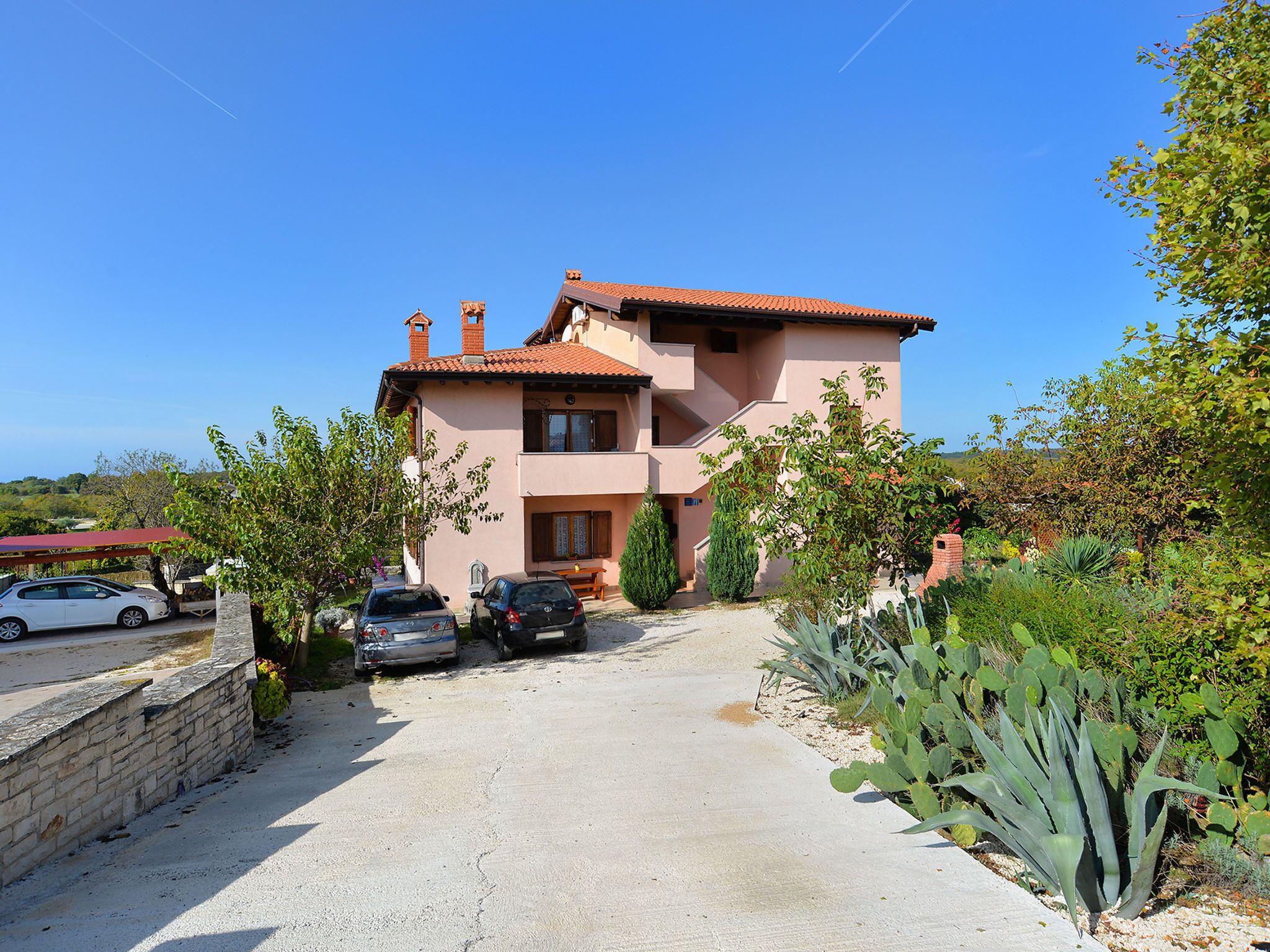 A two-story house with a driveway, parked cars, and a garden with cacti.