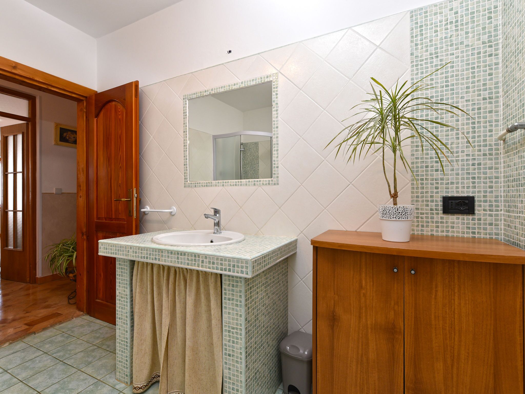 A bathroom with a sink, mirror, potted plant, and wooden cabinet.