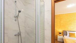 Ein Hotelzimmer mit Dusche, einem Bett mit gelber Bettwäsche und einem Nachttisch mit Lampe.