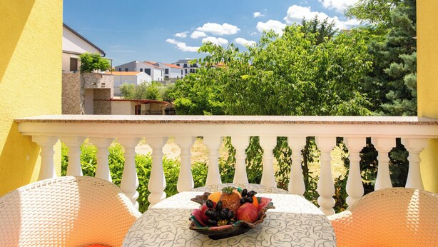 Ein Balkon mit einem Esstisch, Blick auf Gebäude und Bäume, sowie ein weißes Geländer.
