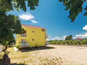 A yellow building with a red roof, a balcony, and a gravel driveway. - Rooms Panorama - 6 by Interhome (Krk/Milohnići)