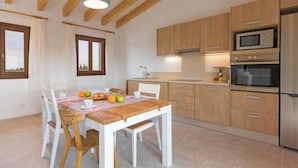 A modern kitchen with wooden cabinets, a stainless steel refrigerator, and a dining area with a wooden table and chairs. - Vacation home Vivot by Interhome (Búger)