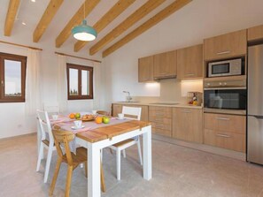 A modern kitchen with wooden cabinets, a stainless steel refrigerator, and a dining area with a wooden table and chairs. - Vacation home Vivot by Interhome (Búger)