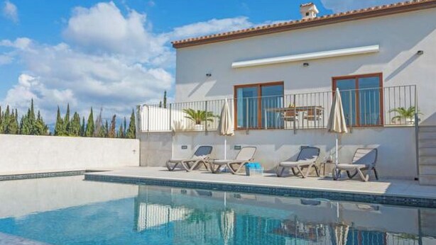 A swimming pool with lounge chairs and umbrellas, a white building with a tiled roof, and a clear sky. - Vacation home Vivot by Interhome (Búger)
